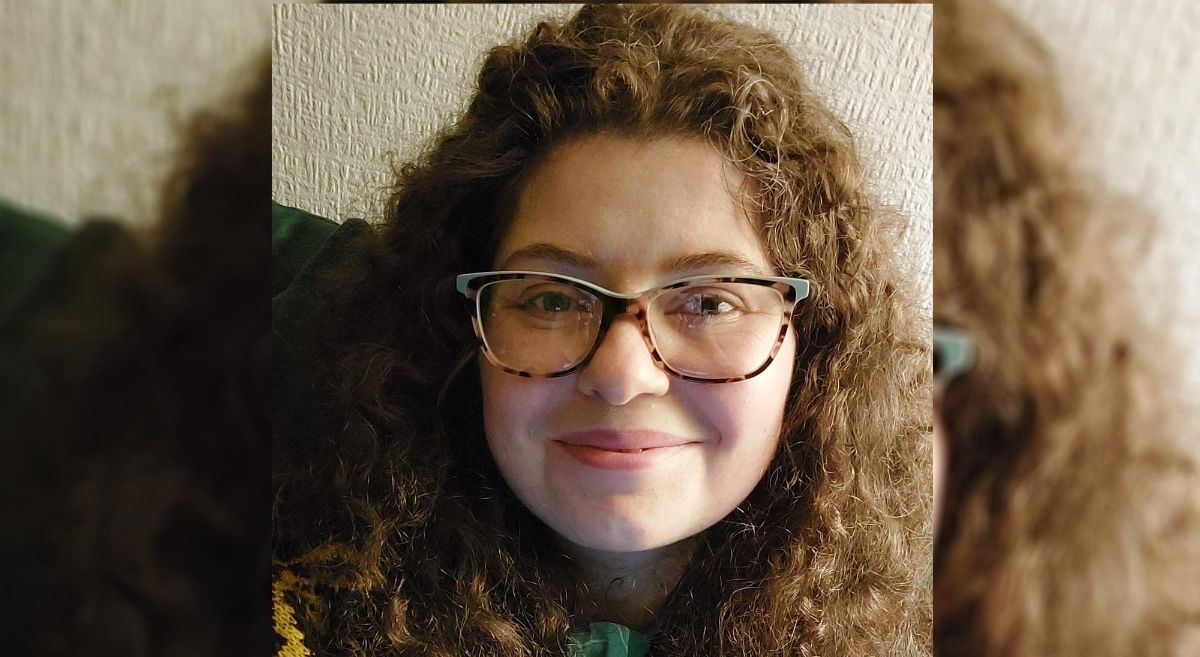 Head shot of female, wearing glasses,  smiling with brown curly long hair.